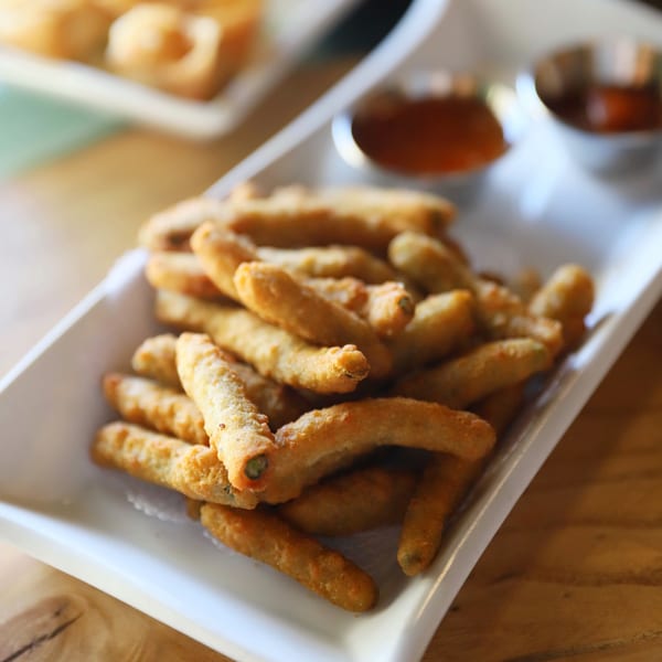 Crispy fried spring rolls, golden brown, served with two dipping sauces on a white rectangular plate.
