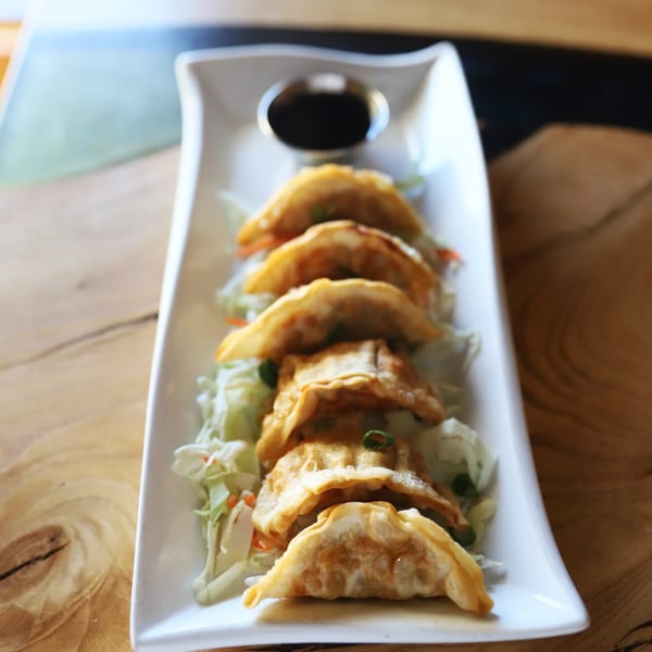 Golden-fried dumplings on a bed of shredded lettuce with a side of soy sauce on a white plate.