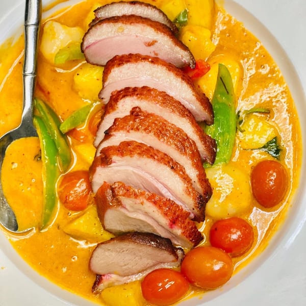 Sliced duck breast in a yellow curry sauce with mango, cherry tomatoes, and green beans.