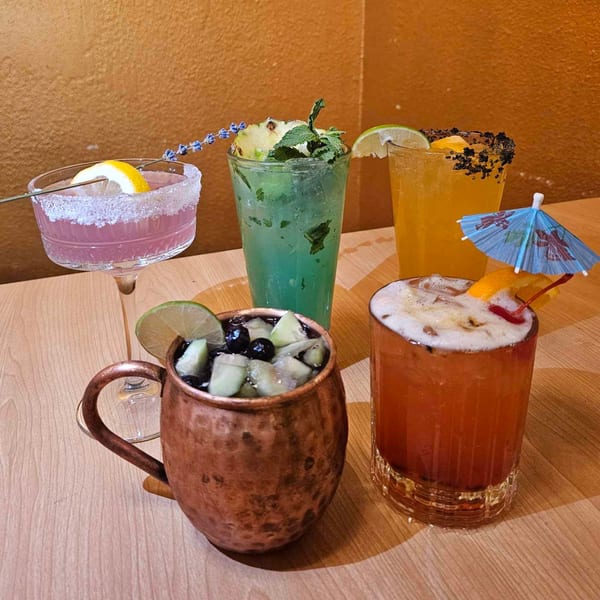 Five colorful, garnished cocktails, including a Moscow Mule, on a wooden table at Taste Asian Fusion Bistro.