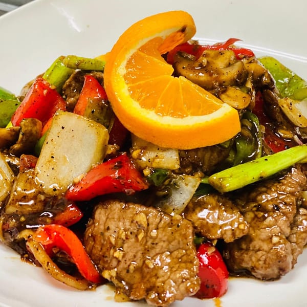 Asian-fusion beef stir-fry with colorful bell peppers, onions, and an orange slice garnish.