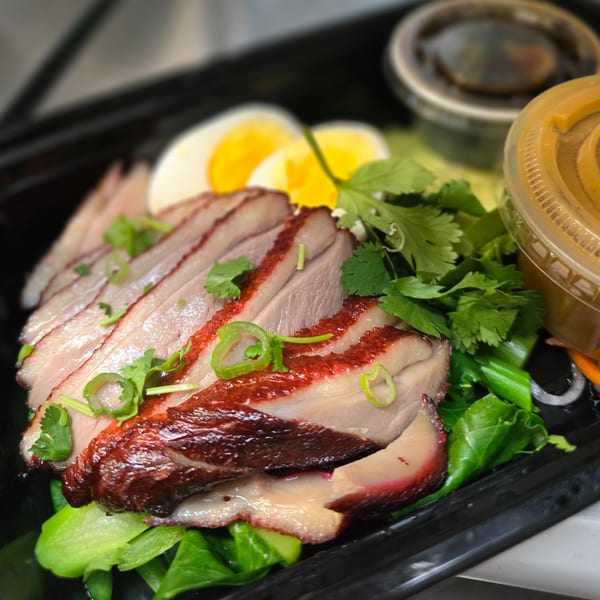 Sliced roasted duck with green vegetables, boiled eggs, and sauces in a black takeout container.