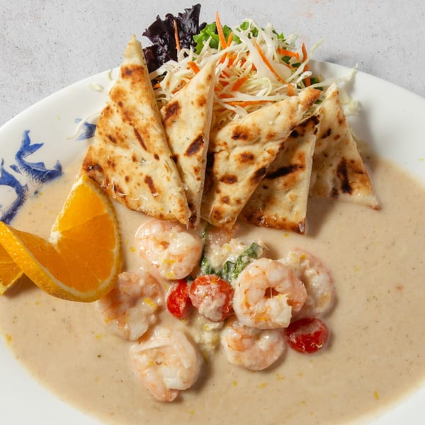 Shrimp in a creamy sauce with cherry tomatoes, spinach, naan bread, and orange slices.