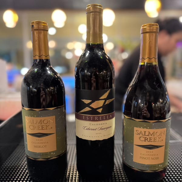 Three wine bottles, including Salmon Creek Merlot and Pinot Noir, and Estrella Cabernet Sauvignon.
